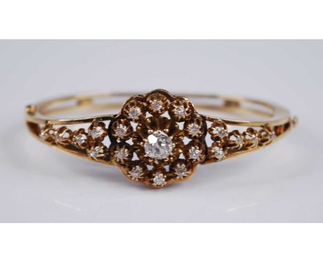 A yellow metal diamond set hinged bangle, the Edwardian style flower head openwork setting containing a claw-set centre old r