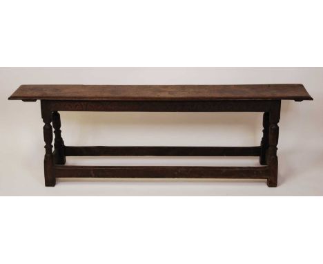 An 18th century and later joined oak long bench, having a single plank top and carved detail frieze, raised on ring turned an