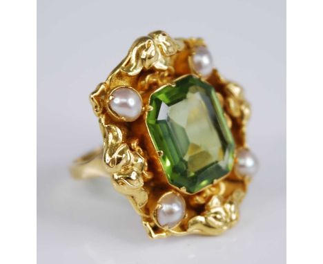 A yellow metal, peridot and pearl dress ring, comprising an emerald cut peridot within an ornate scrollwork surround set with