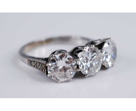 A white metal diamond three stone ring, comprising three round brilliant cut diamonds in claw settings, with three 1.1mm mele