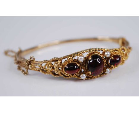A Victorian style 9ct gold, garnet and seed pearl hinged bangle, the three cabochon garnets dispersed with four seed pearls a