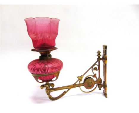 A VICTORIAN WALL MOUNTED OIL LAMP,  the brass bracket in the Aesthetic taste, with cranberry glass reservoir and shade