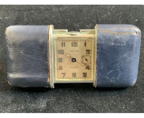 A Movado Ermento Swiss made travel clock in leather case. Patent Swiss made Fab Suiss Modavo Factories marked to stand. Seria