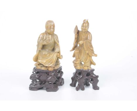 Two Chinese carved hardstone figures of immortal godsEach carved on a rocky outcrop, wearing flowing robes, holding a fan and