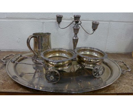 A large silver plated tray, a pair of wine coasters in the form of a cart, a plated tankard with copper bottom and a candelab