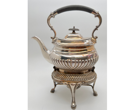 An Edwardian silver plated spirit kettle of reeded design, on hinged stand raised on 4 padded feet. Ebonised handle and lid f