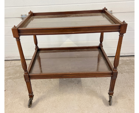 A vintage dark wood tea trolley with turned legs and glass inserts to shelves. 