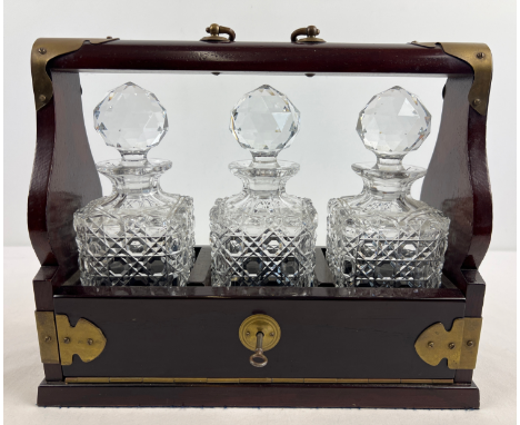 A vintage dark wood brass banded 3 decanter tantalus complete with key. With 3 matching hobnail cut lead crystal decanters wi