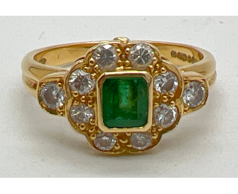 An 18ct gold diamond and emerald dress ring. Central square cut emerald surrounded by 8 round cut diamonds with one small dia