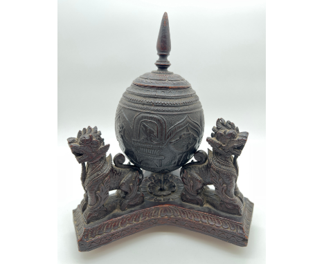 A vintage highly carved coconut shell canister raised on a carved wooden tripod stand with Foo dog rests (a/f). Carved wooden