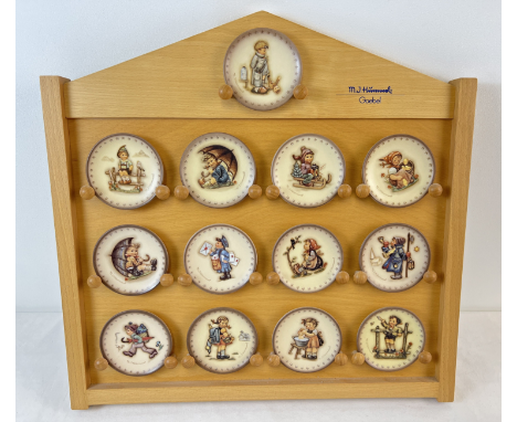 A collection of 13 assorted M.J. Hummel Goebel ceramic miniature plates together with a wooden wall display stand. 11 boxed a