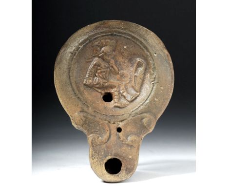 Roman, Imperial Period, ca. 1st century CE. A mold-made oil lamp with a projecting spout and a slightly concave discus. On th