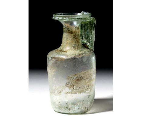 Roman, ca. 2nd to 3rd century CE. A sizable, translucent green glass jug with a cylindrical body extending to a tubular neck 