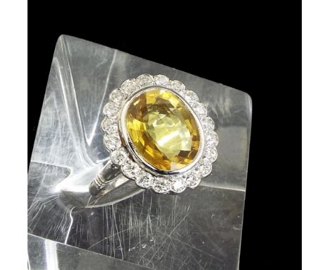 Large fancy yellow sapphire and diamond oval cluster ring in 18ct white gold, the sapphire 4.80ct approx within a surround of