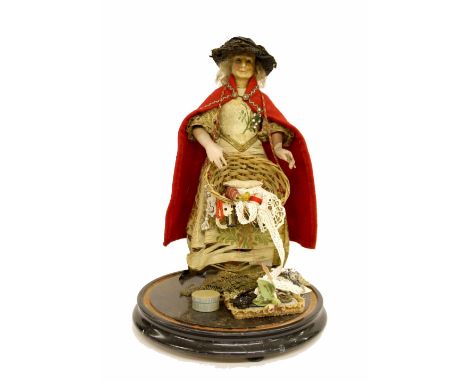 Victorian wax Peddler doll  under a glass dome, the doll wearing a cloak and dress displaying goods in a wicker basket, the d