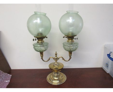 An ornate double brass oil lamp with pale green cushion reservoirs and acid etched globe shades 