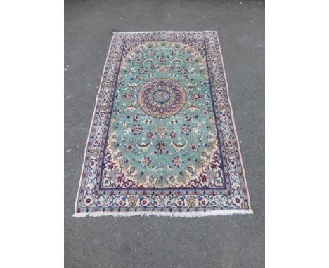 A handmade Iranian Ispehan floor rug with central floral medallion on a light green and cream ground. Size 187 x 117 cm.
