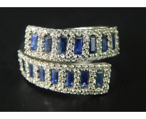 An 18ct white gold crossover ring, set with baguette cut sapphires, surrounded by tiny diamonds, marks to inner band ZEN 750,