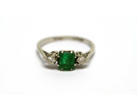 An emerald and diamond ring, the rectangular step cut emerald flanked by brilliant cut diamonds weighing a total of approxima