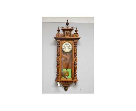 A Viennese walnut and beechwood wall clock, the cornice with mask, leaf decoration and turned finials, above an enamelled rom