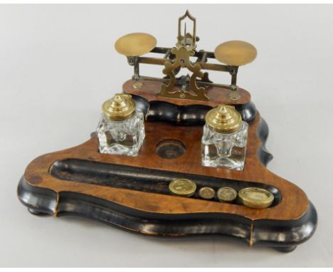An Edwardian walnut and ebonised desk stand, with weighing scale, inkwells and space for pens, on a shaped base, terminating 