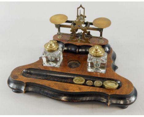 An Edwardian walnut and ebonised desk stand, with weighing scale, inkwells and space for pens, on a shaped base, terminating 