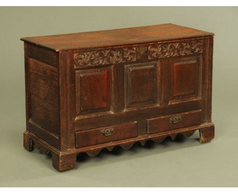 An 18th century oak coffer, with carved frieze above three panels and fitted with two drawers beneath and with shaped apron a