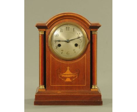 An Edwardian inlaid mahogany mantle clock, with silvered dial and three train movement flanked by pillars and raised on a ste