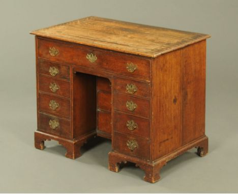 A George III oak kneehole desk, with hinged top with recessed book ledge and with pullout candle sconces, the frieze drawer w