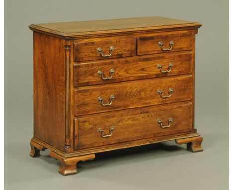 An oak chest of drawers of Georgian style, with crossbanded top and quartered fluted columns to front on ogee bracket feet.  