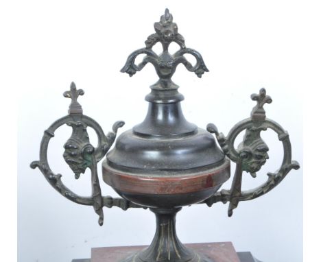 An early 20th century slate mantle clock having a urn shaped finial atop a stepped body, ebonised clock face flanked by lions