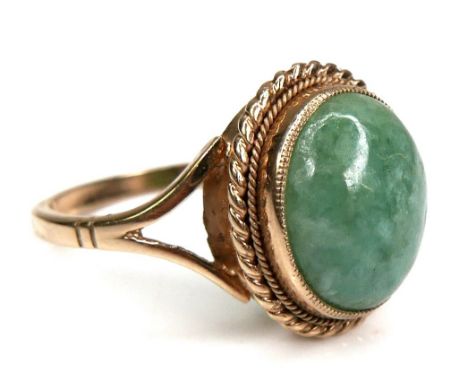 A 9ct yellow gold and jade set ring, the oval cabochon cut jade 11.8 by 9.8mm, in rub over setting with milgrain edge, and ro