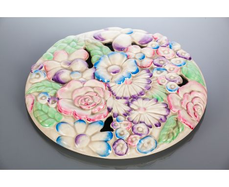 CLARICE CLIFF FOR WILKINSON WALL PLAQUE
of circular form with moulded flowers in shades of pink, purple and blue, with blue p