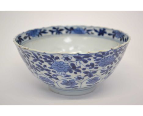A Chinese porcelain bowl Kangxi with blue and white design of stylised flowers beneath a wavy rim and floral boder with Kangx