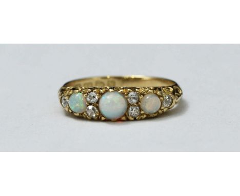 A late Victorian 18ct gold, opal and diamond ring, with scroll-carved top set with three round graduated opals interspersed w