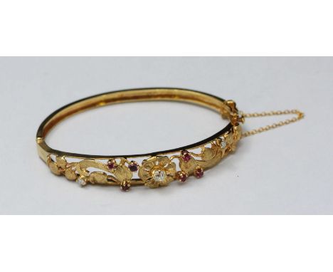 A 9ct gold hinged bangle bracelet, the open floral and scrolling foliate carved top claw-set with three diamonds and six rubi