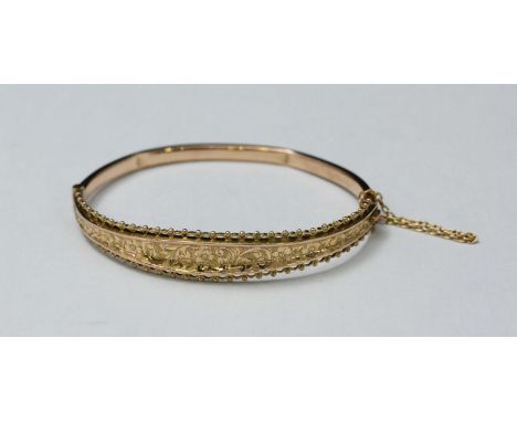 An early 20th century 9ct gold hinged bangle, with scrolling foliate-engraved and pierced ball-finial edged panel, with safet