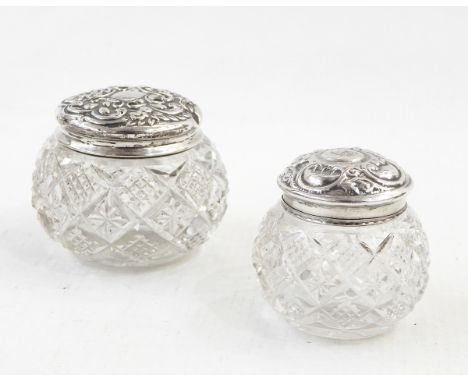 A pair of cut glass dressing table jars of compressed circular form, with embossed silver covers and another, similar 