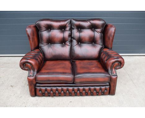 A modern Chesterfield style two-seater sofa with button-back design in oxblood red. In good functional condition with some si