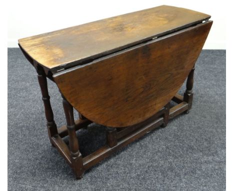 AN EARLY NINETEENTH CENTURY OAK DROP-LEAF GATE LEG TABLE having shaped apron above corner turned supports with floor stretche