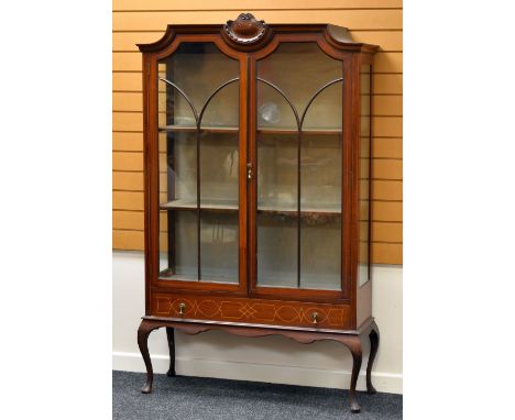 AN EDWARDIAN INLAID MAHOGANY CABINET standing on bow supports with base drawer and two shaped glazed doors and having a shell