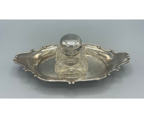 Edwardian silver mounted glass inkwell on oval stand with serpentine border, on four bun feet by William Hair Haseler, Birmin