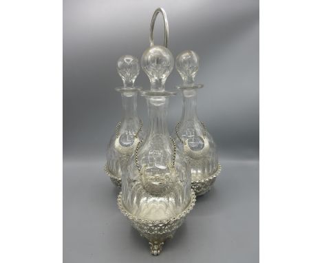 Early 20th century EPNS decanter stand, with three facet cut glass mallet shaped decanters, on scroll feet with loop handle, 