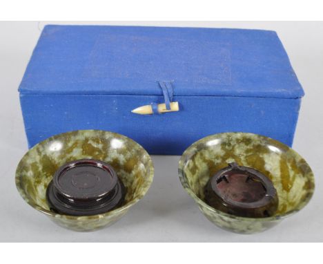 A pair of spinach jade bowls, each of flared form in mottled green hues, with a pair of carved wooden stands, in presentation