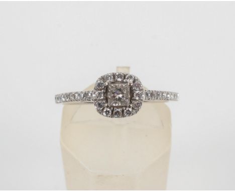 A white metal diamond cluster ring. Principally set with a princess cut diamond and finished with round brilliant cut diamond