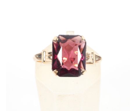 A yellow metal single stone ring. Set with a rectangular cushion cut rhodolite garnet. No hallmark - stamped 10K. Size: L 2.0