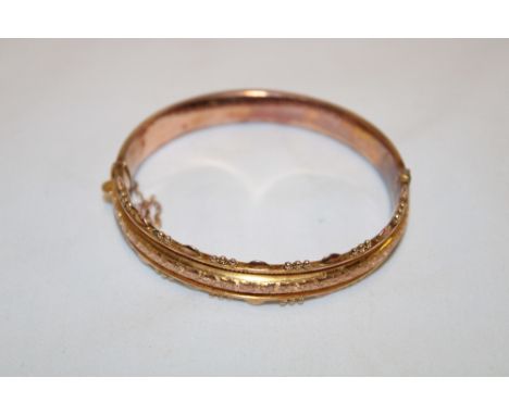 A 9ct gold oval bangle with raised scroll decoration (11.2g)