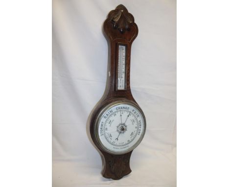 An aneroid barometer with ceramic circular dial below thermometer in carved oak case
