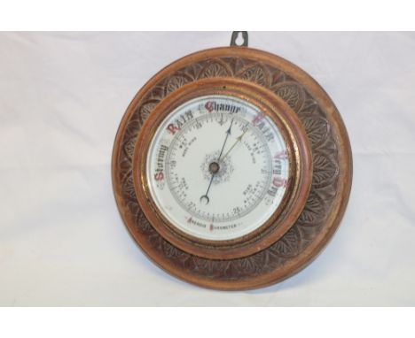An old aneroid barometer with ceramic circular dial in carved oak circular case