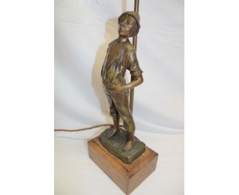 A bronzed spelter table lamp in the form of a young boy beneath a scroll lantern with glass shade on a rectangular wooden bas